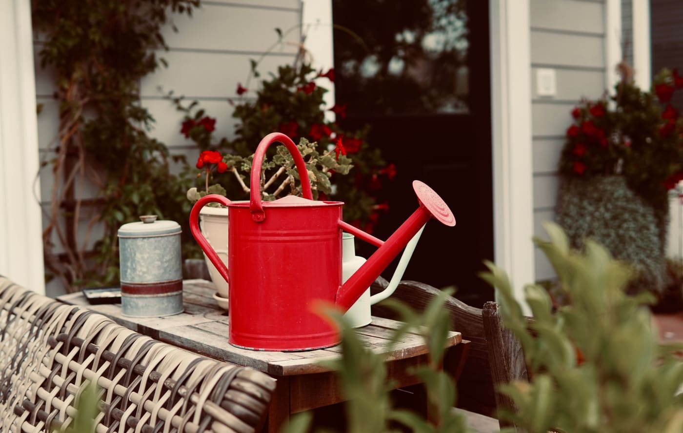 A red watering can on a patio table among flowers