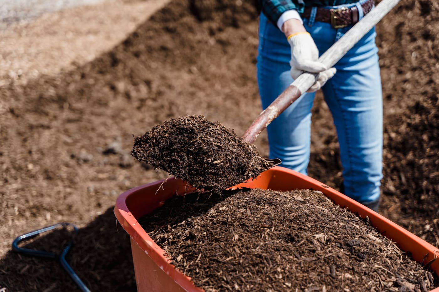 Someone shoveling compost into a red tub from a large pile